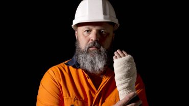 A male worker with a hand injury, on a black background with copy space.